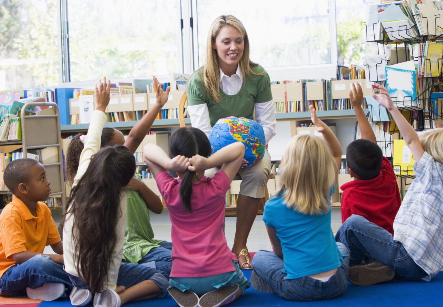 Elementary teacher with a globe and students raising their hands