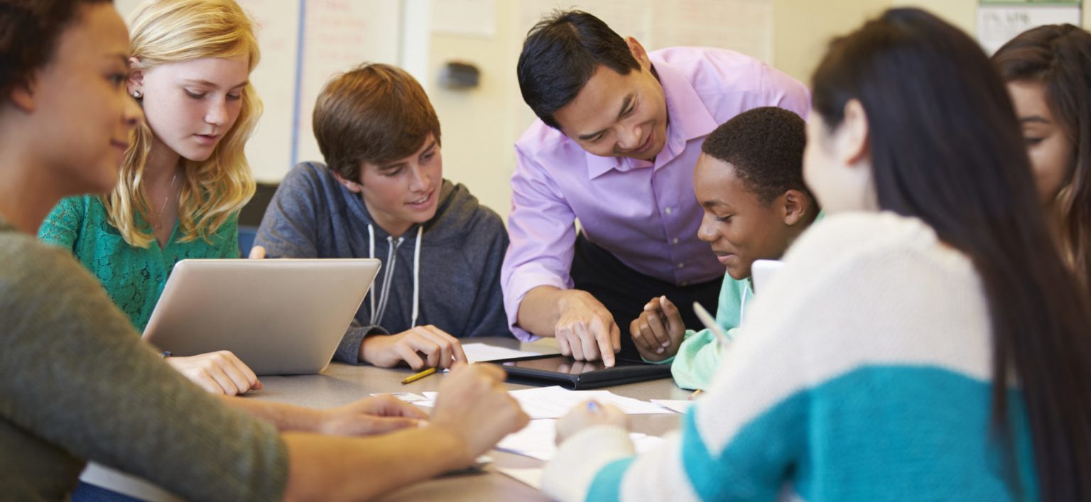 Teacher helping high school students with a group project