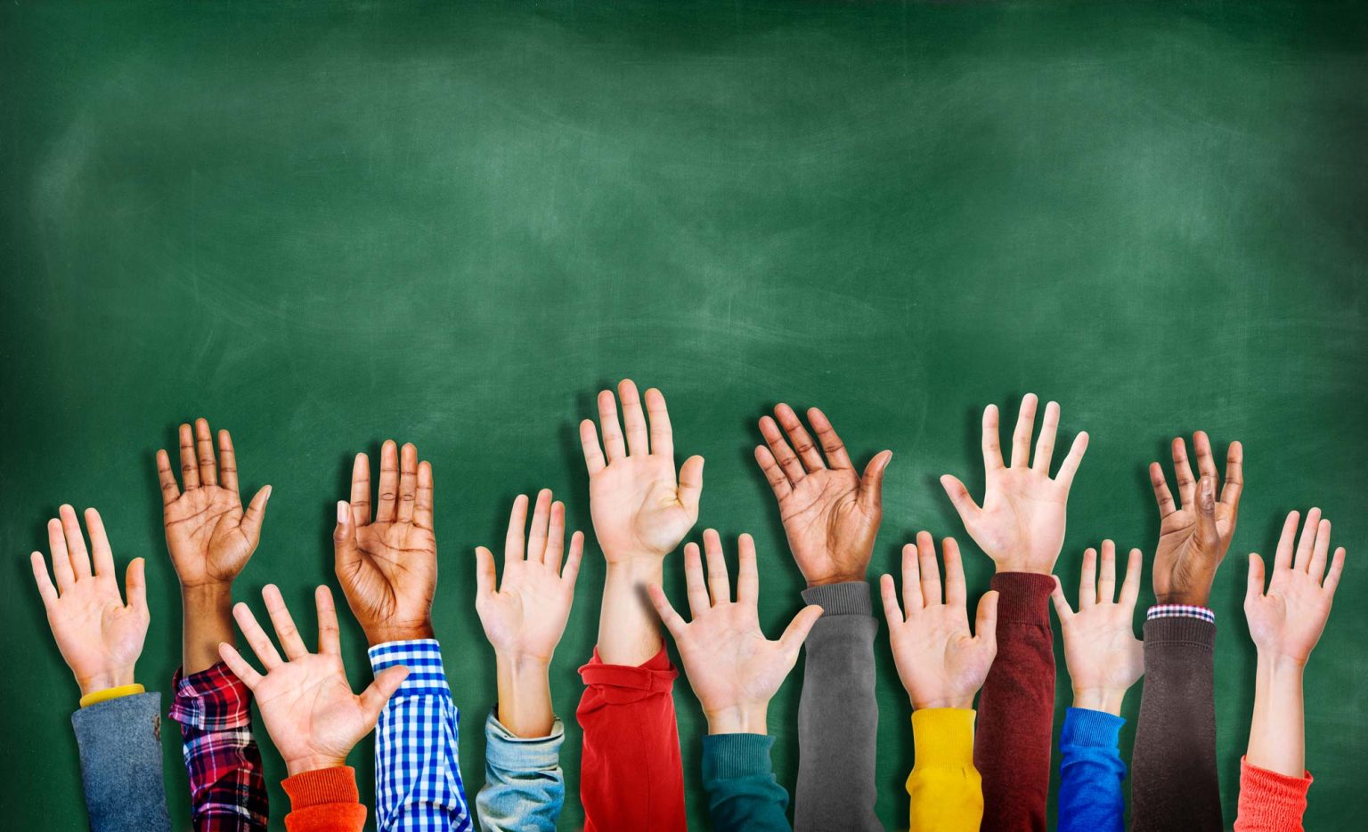 Raised hands of students in front of a chalkboard